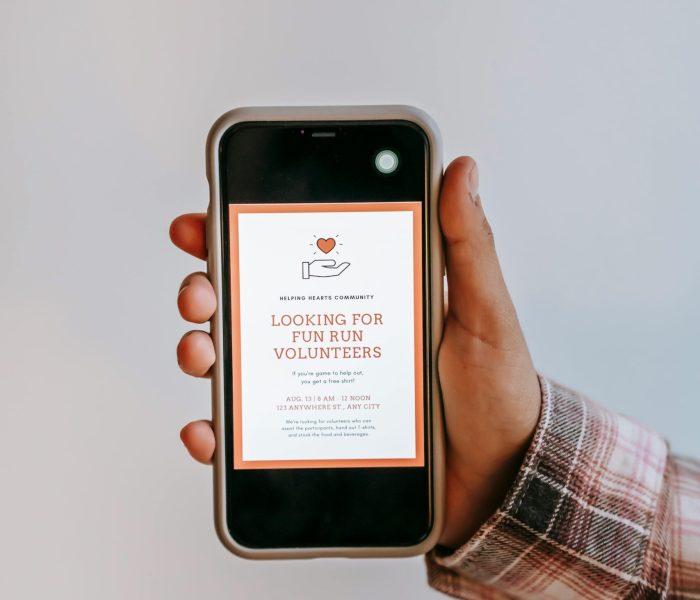 Crop anonymous person holding smartphone in hand and demonstrating screen with app with invitation to be volunteer on gray background